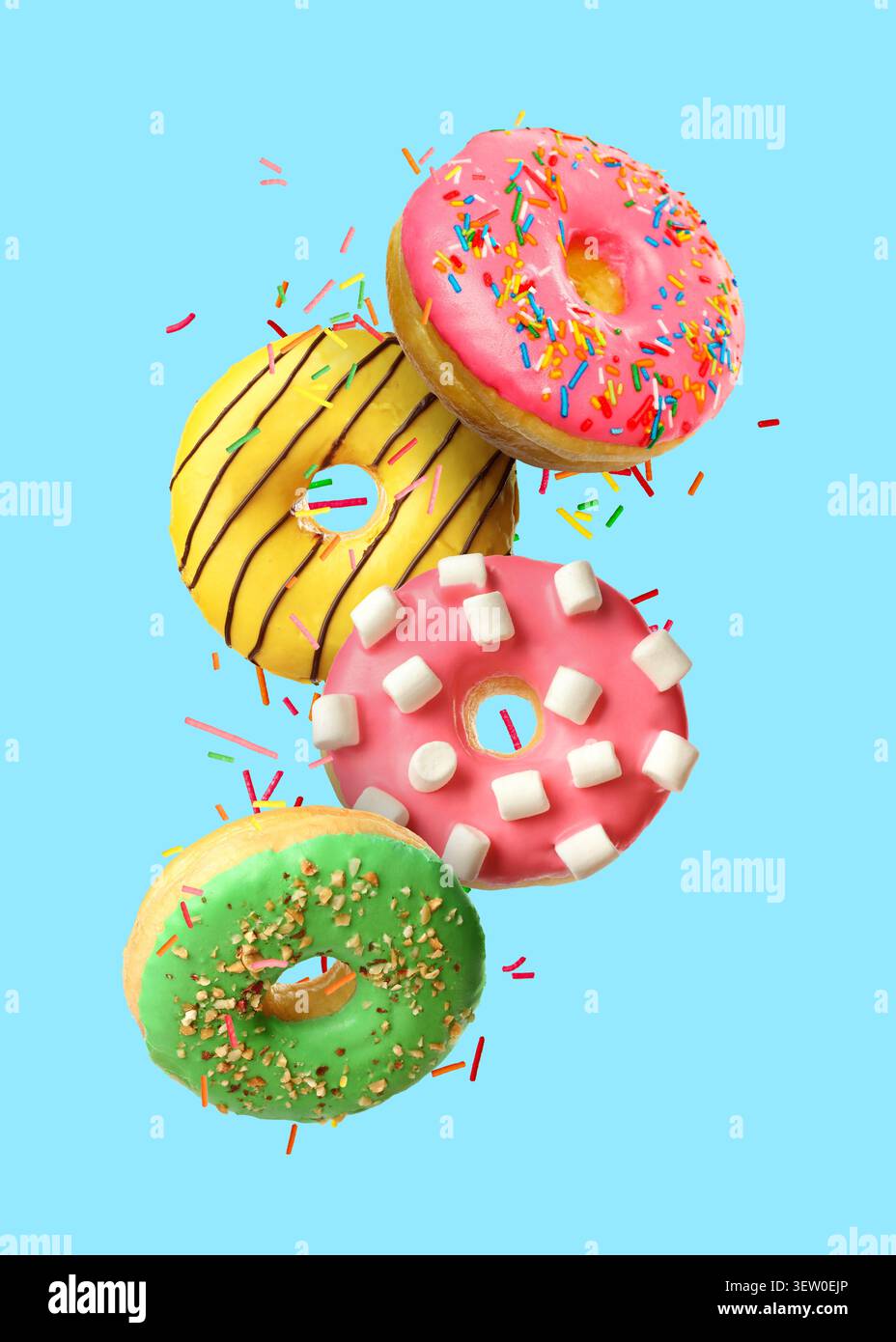 Sweet donuts and sprinkles falling on light blue background Stock Photo