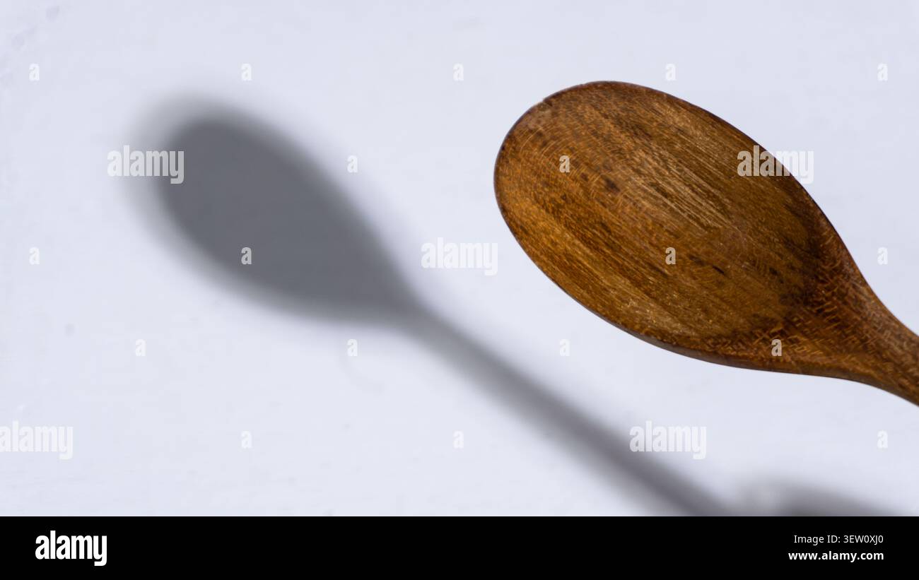 Close up view of a smooth carved wooden spoon bowl suspended diagonally over a solid white background, casting a distinct soft rounded shadow that hig Stock Photo