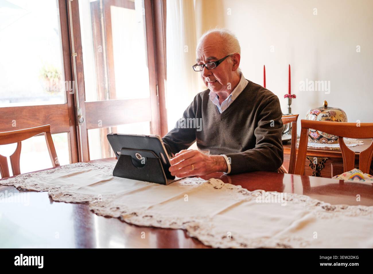 Senior man sitting at a table interacting with a tablet computer Stock Photo