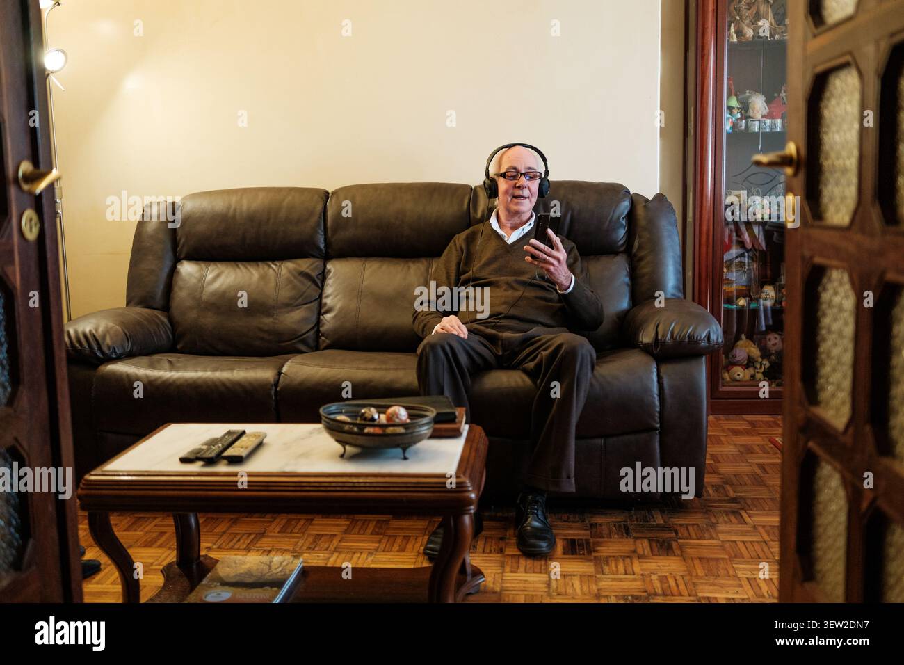 Senior man listening to music on headphones while using smartphone at home Stock Photo