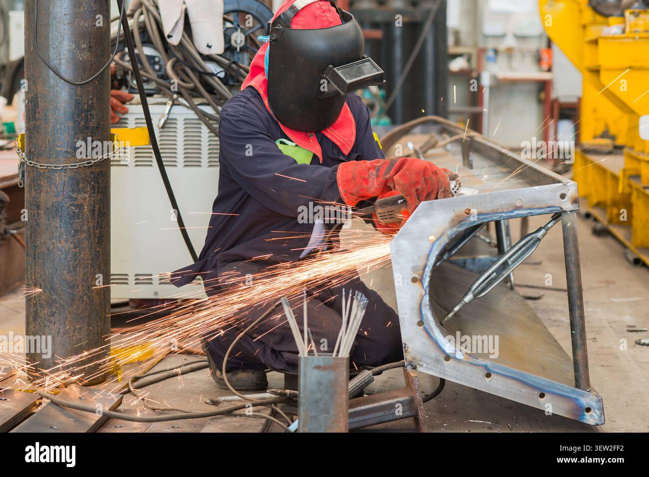 Man with protective gear working on a screw conveyor trough using an angle grinder. Stock Photo