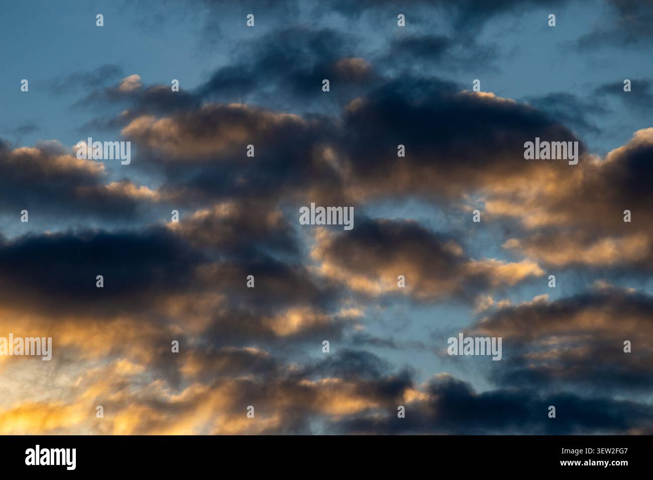 Dark brooding clouds lit from below by golden light against a blue sky at sunset Stock Photo