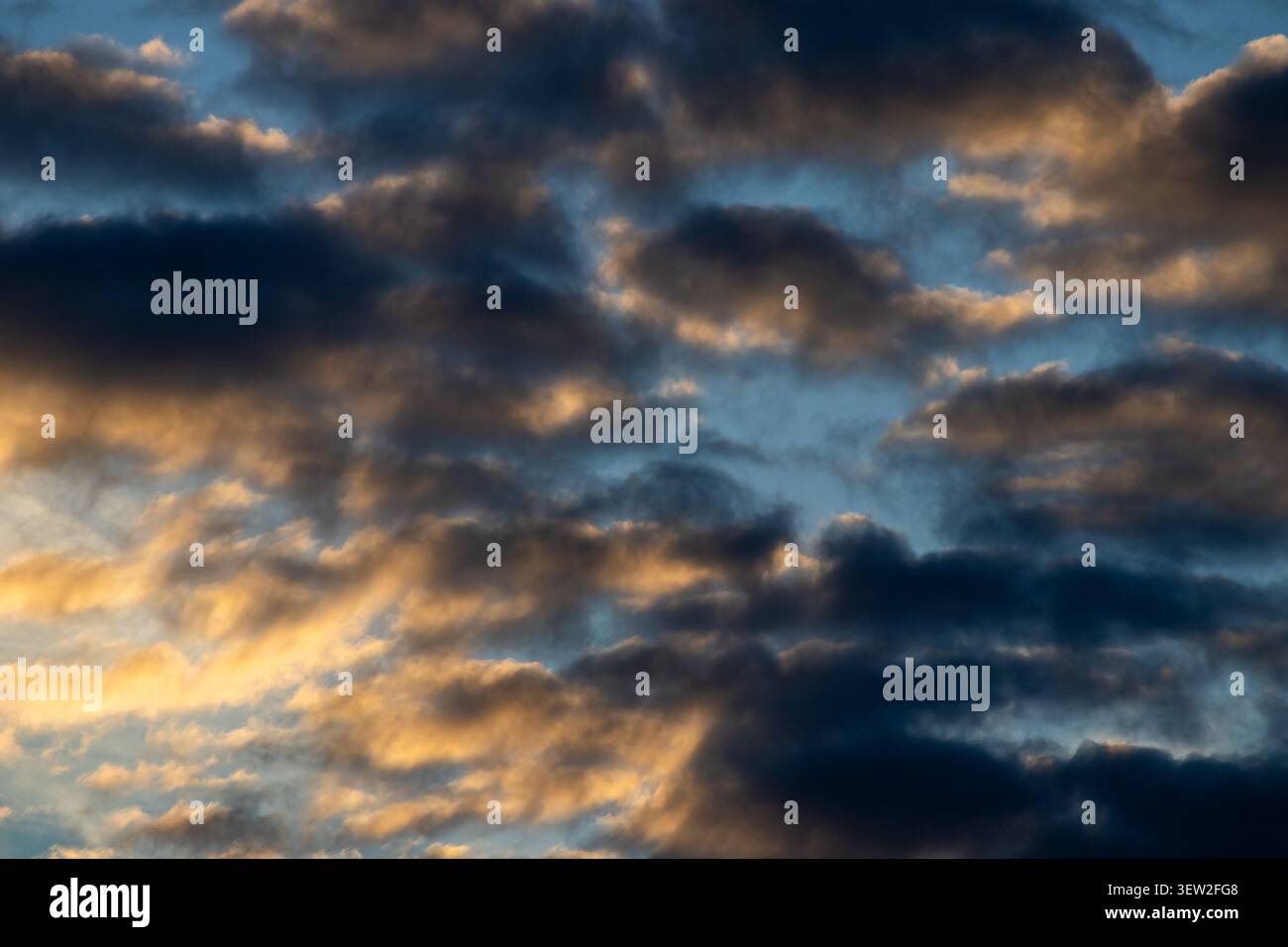 Dark brooding clouds lit from below by golden light against a blue sky at sunset Stock Photo