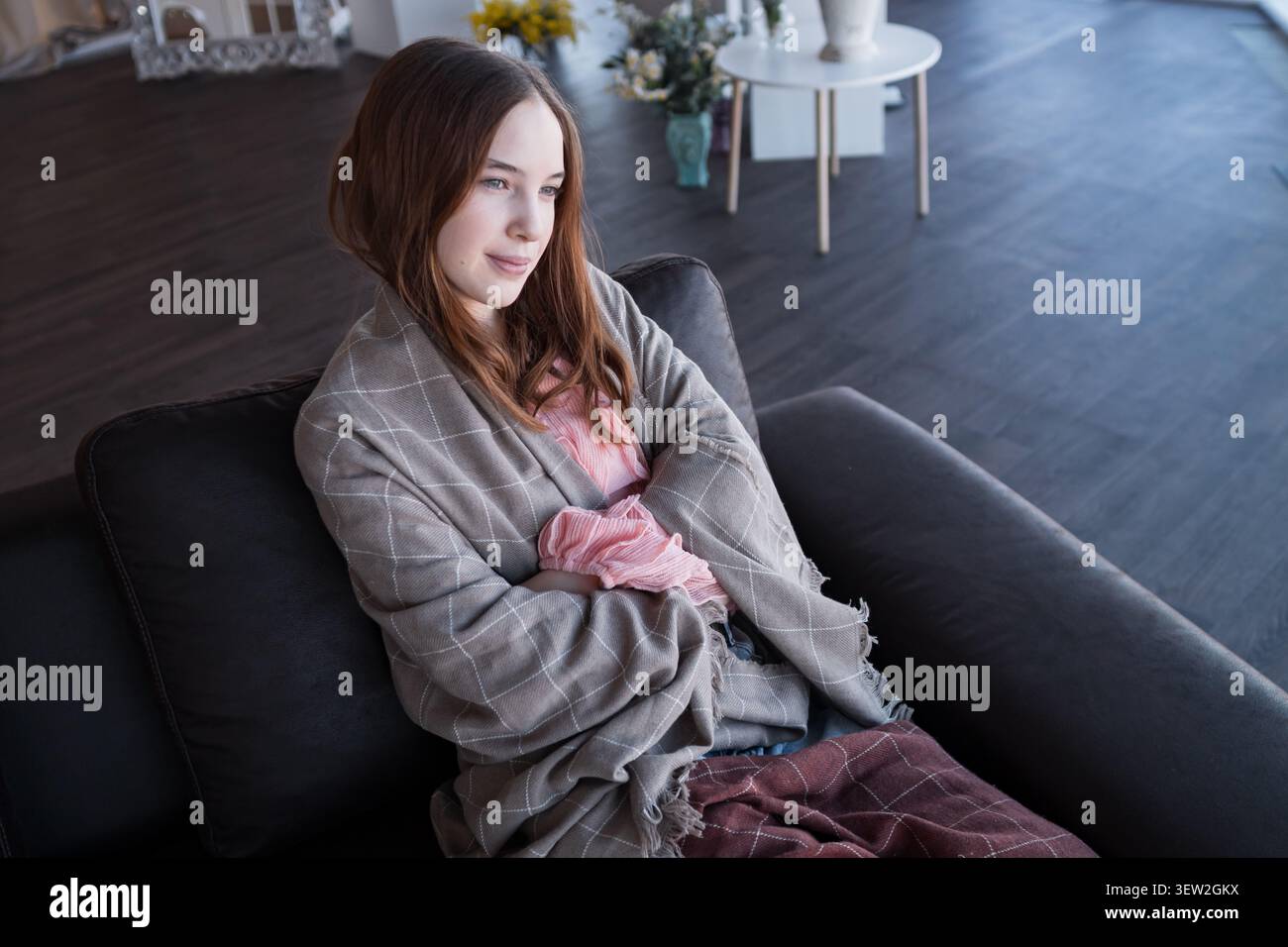 Young woman day dreaming on couch wrapped in blanket Stock Photo