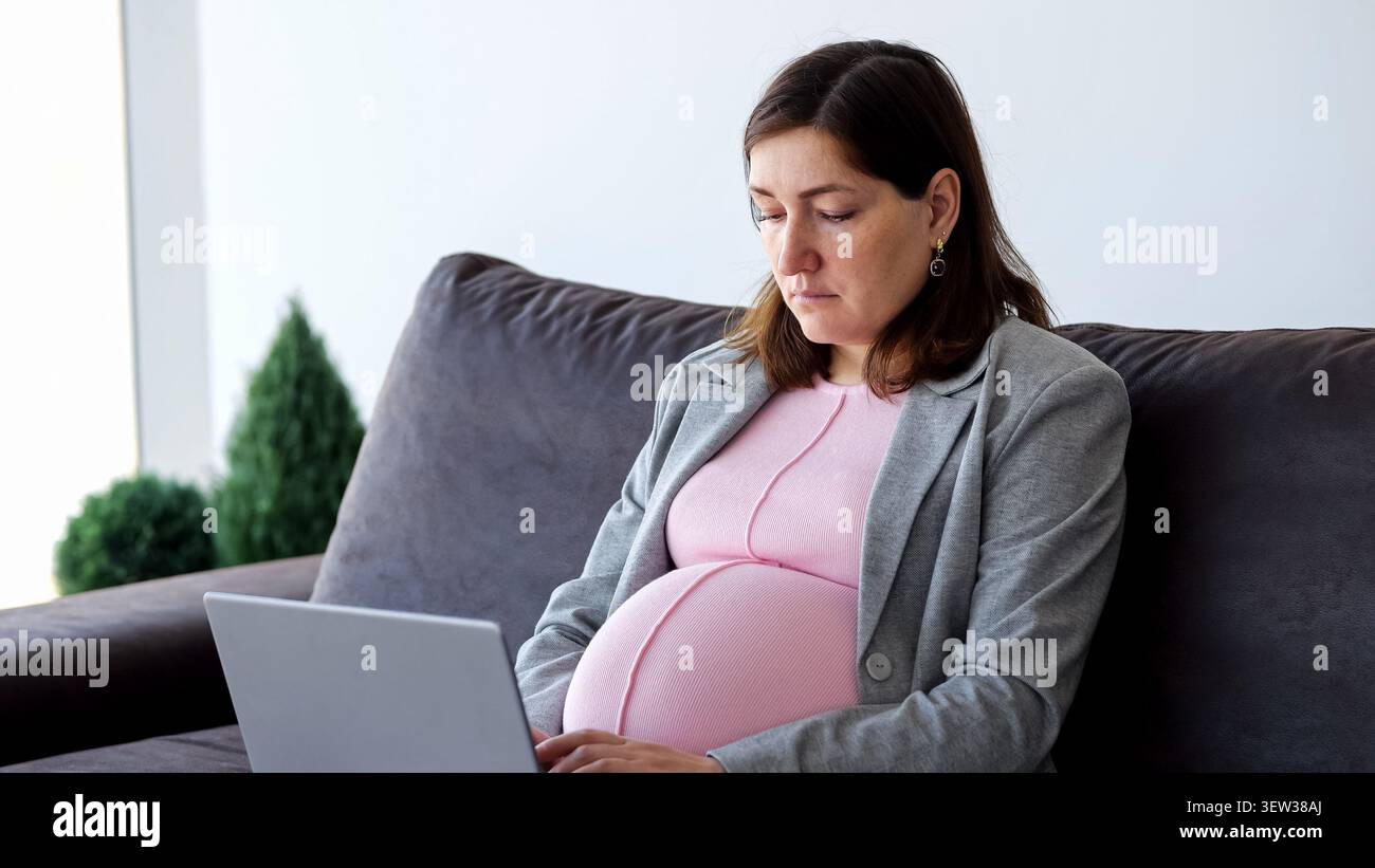 Pregnant woman working from home on laptop Stock Photo
