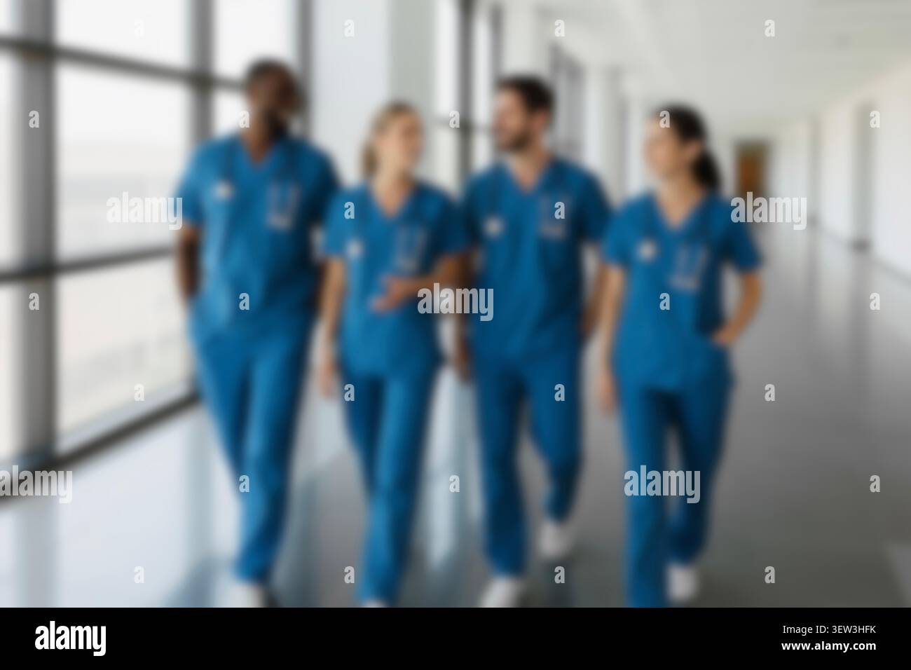 Blurred healthcare team walking in a hospital hallway. Diverse confident doctors, nurses in scrubs smiling, collaborating, and discussing patient care Stock Photo