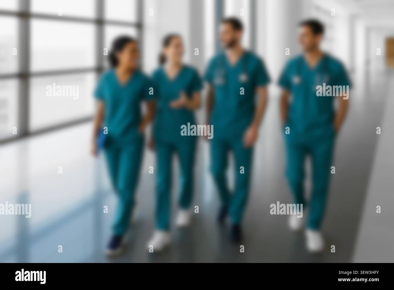 Blurred healthcare team walking in a hospital hallway. Diverse confident doctors, nurses in scrubs smiling, collaborating, and discussing patient care Stock Photo