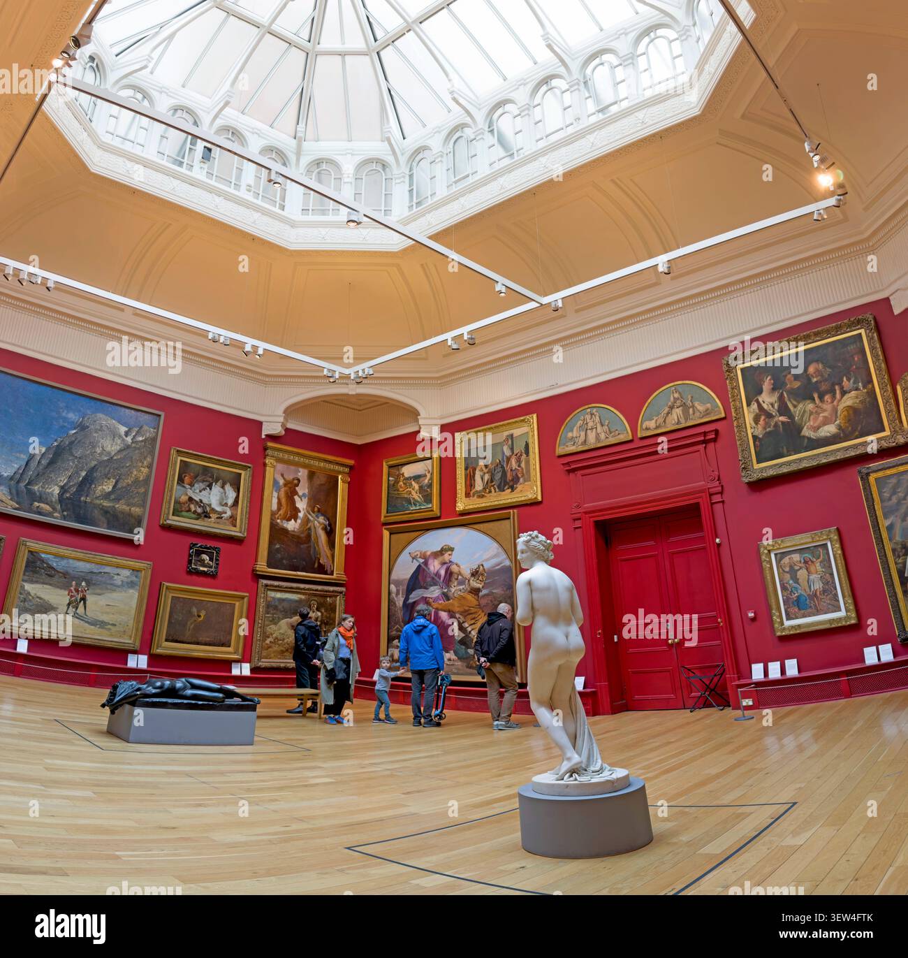 Historic Paintings, sculpture and visitors inside the red-walled Central Court Gallery at Leeds Art Gallery, West Yorkshire Stock Photo