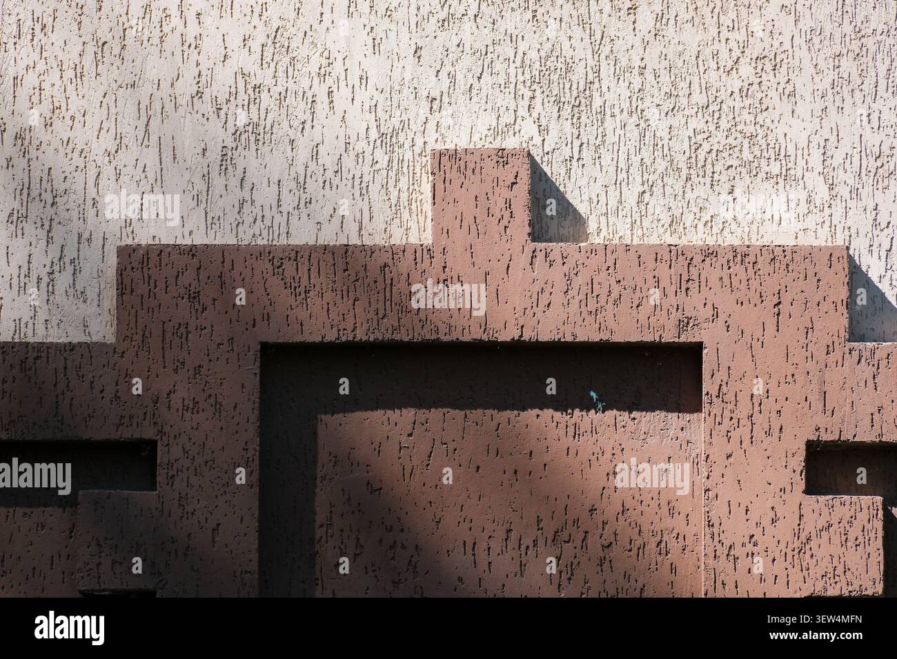 Sunlight casts shadows on a textured wall displaying geometric forms and colors. Stock Photo
