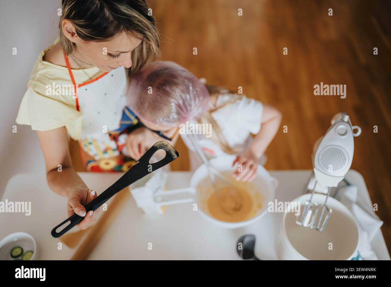 Mom and child baking together at home mixing batter in a bright kitchen while wearing aprons Stock Photo