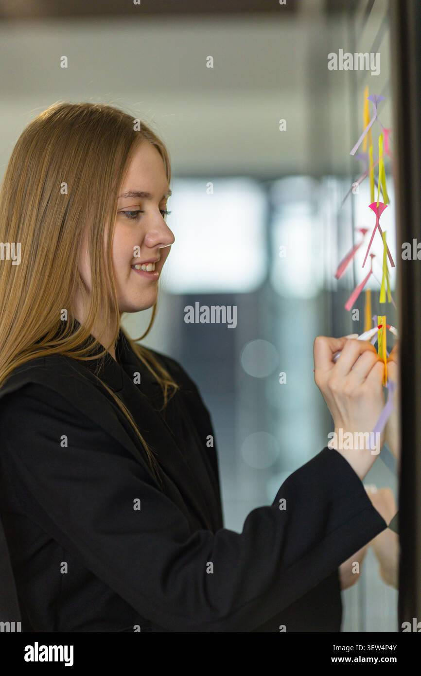 Young businesswoman writing on sticky notes during project planning Stock Photo