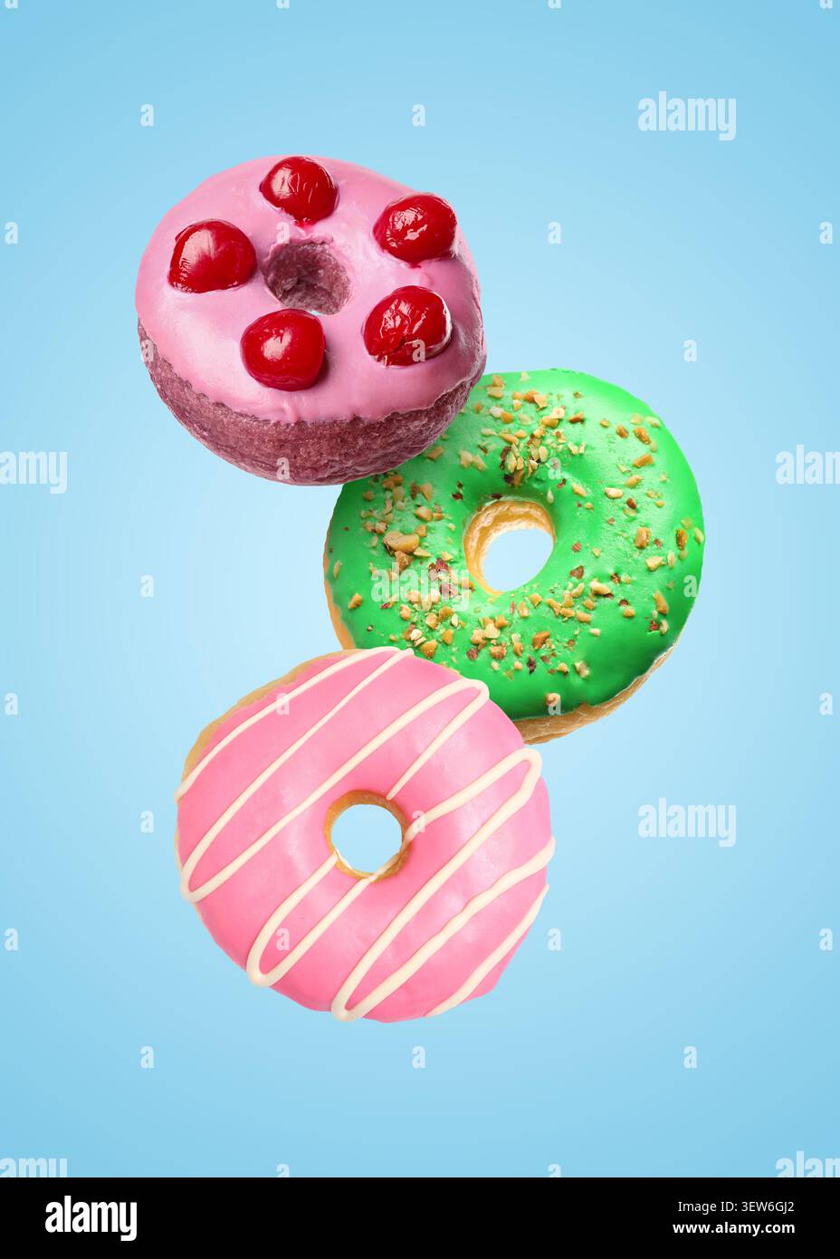 Yummy donuts covered with icing falling on light blue background Stock Photo