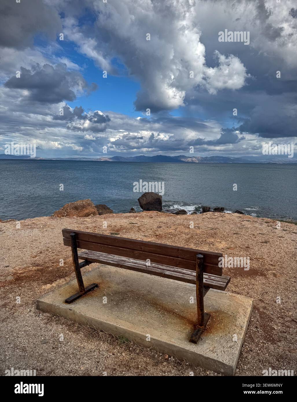 Empty wooden bench overlooking calm sea beneath dramatic storm clouds - Smartphone Captured Stock Image