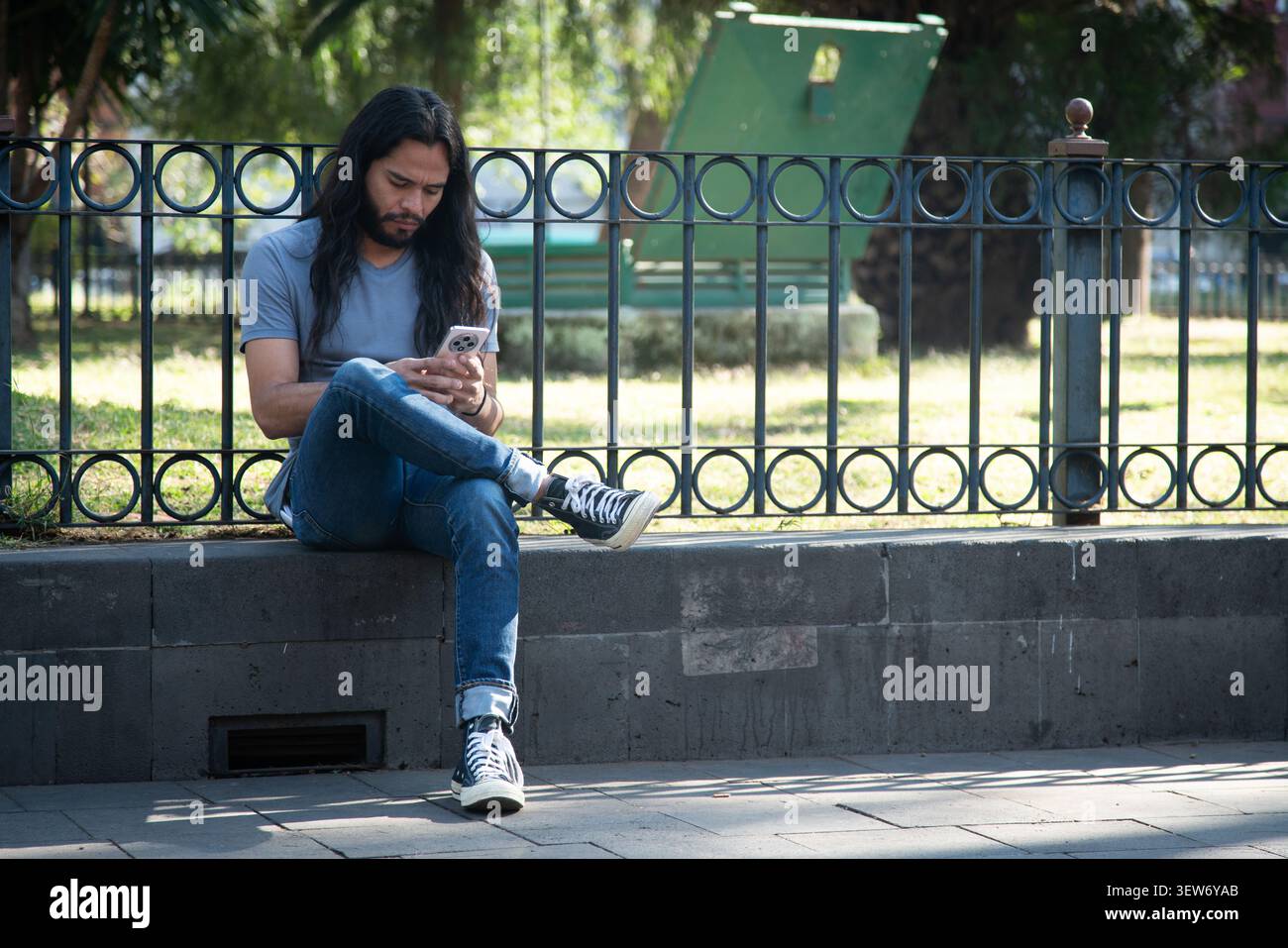 Young man using smartphone sitting on park ledge Stock Photo