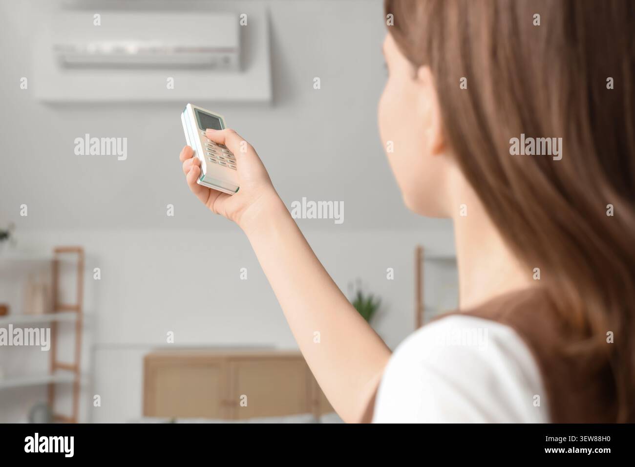 Woman using remote control to operate air conditioner Stock Photo