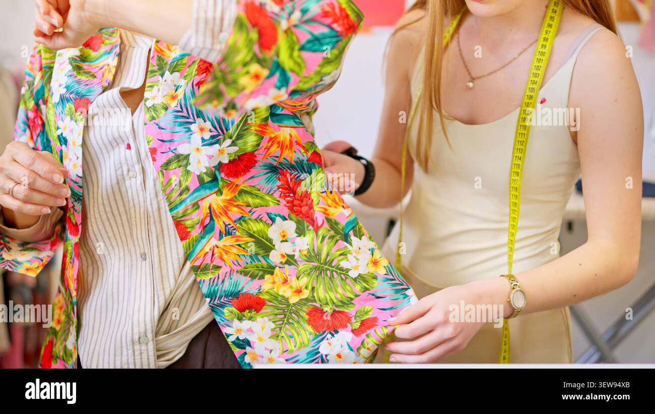 Designer fitting floral garment on customer in creative workshop Stock Photo