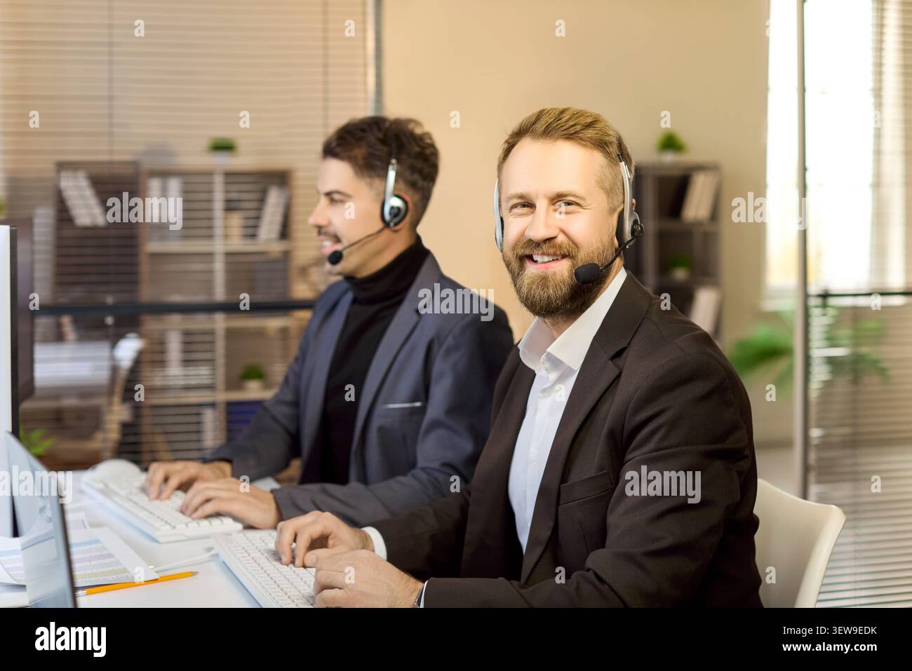 Happy customer service representatives using headsets at computers in bright office Stock Photo