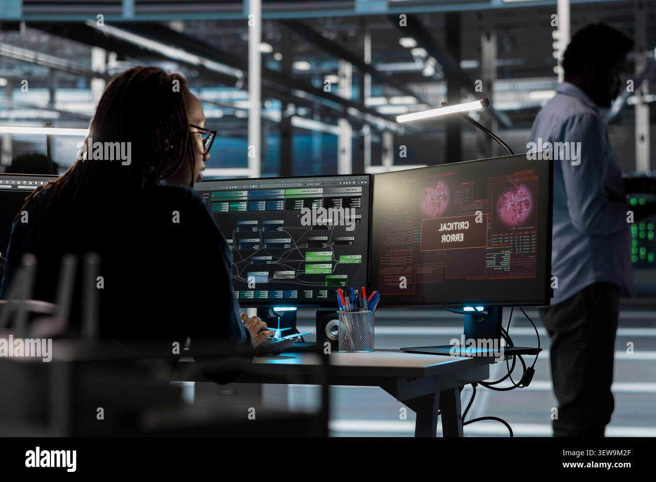 Concerned female IT worker reviews warning messages in a data center while troubleshooting errors affecting equipment performance. Stock Photo