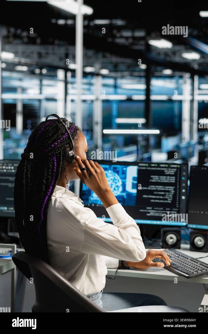 IT expert provides technical support from a data center using a headset while troubleshooting client server issues. Stock Photo