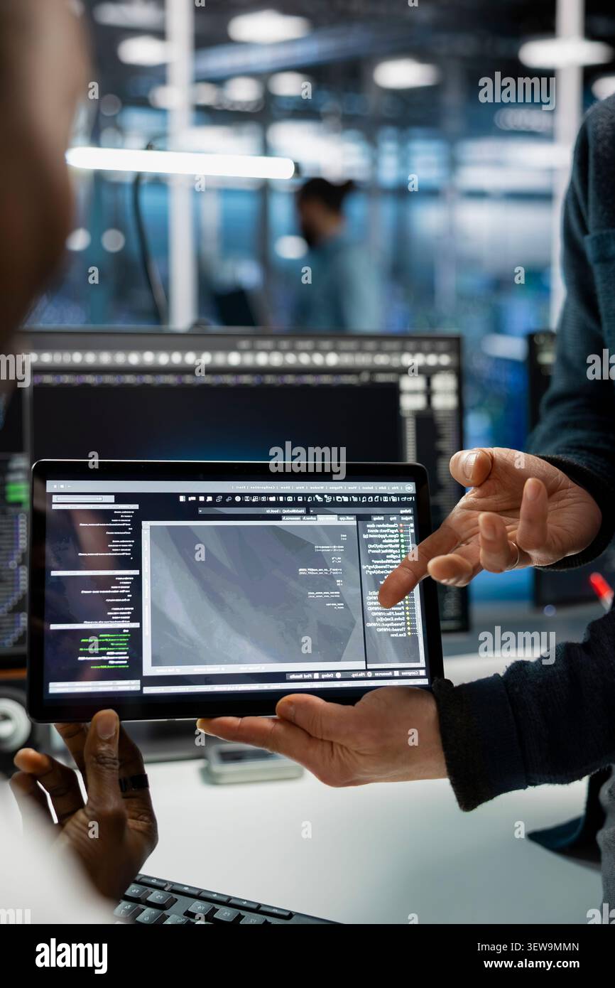 Data center programmers use a digital tablet in a data center to deploy software updates, configure hardware, and support reliable operations. Stock Photo