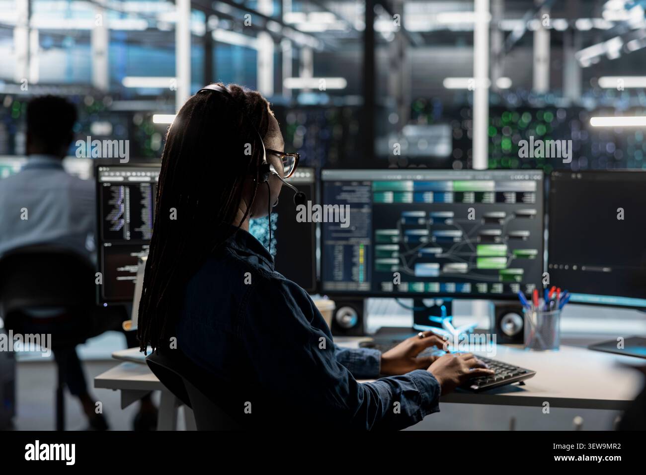 IT expert provides technical support from a data center using a headset while troubleshooting client server issues. Stock Photo