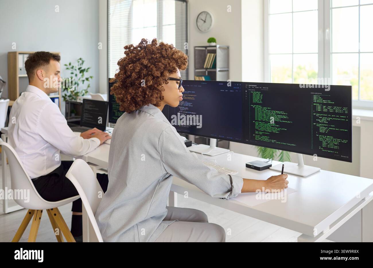 Female developer coding at multi monitor setup in contemporary collaborative office Stock Photo