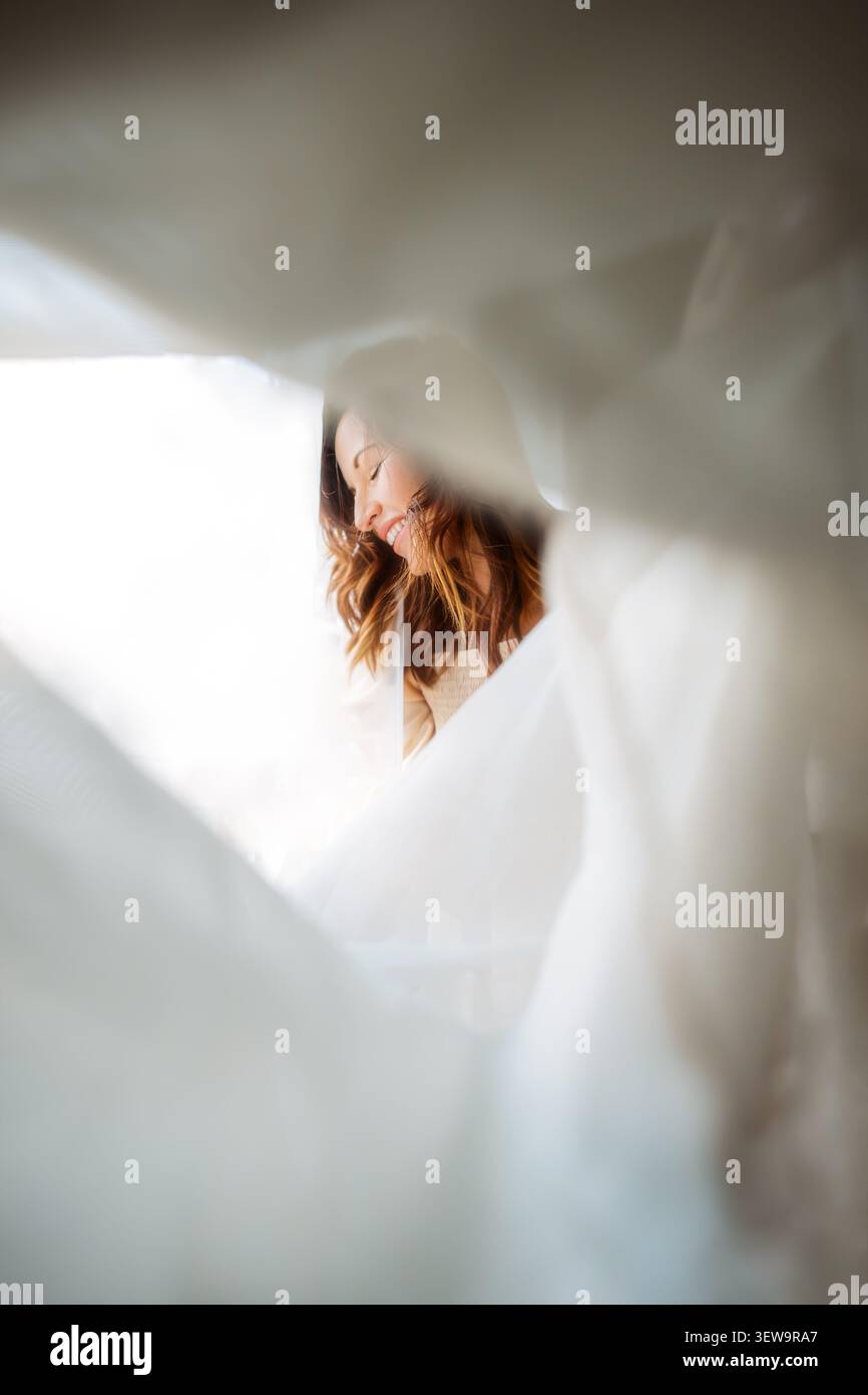 Happy woman smiling from behind white fabric Stock Photo
