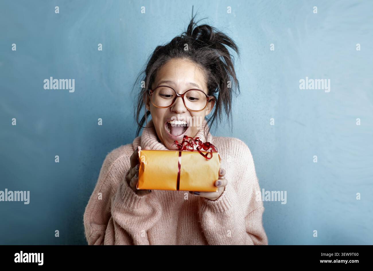 Surprised young woman with glasses holding a gift Stock Photo