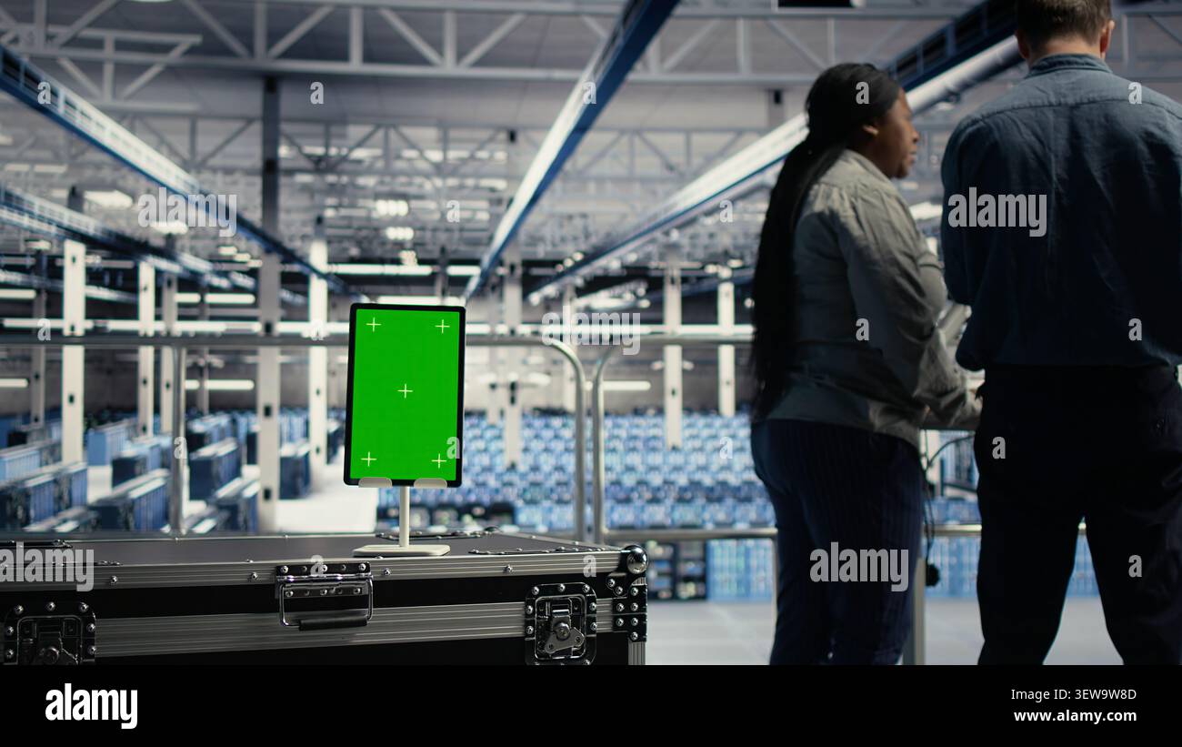System administrator uses a green screen tablet in a server room for AI workflow and screen replacement. Stock Photo