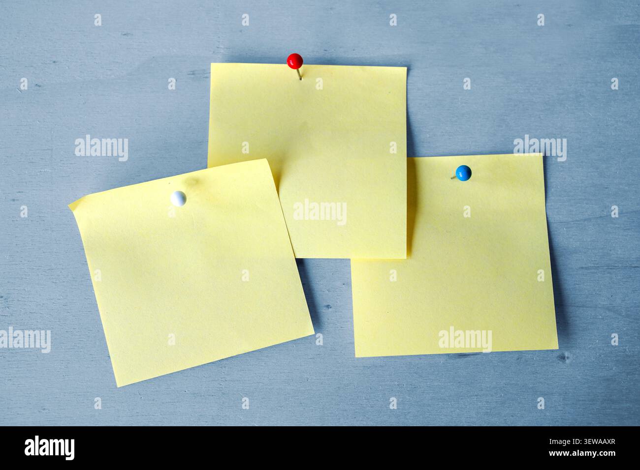 Three blank yellow sticky notes with attached with pins to a blue wooden wall, copy space Stock Photo