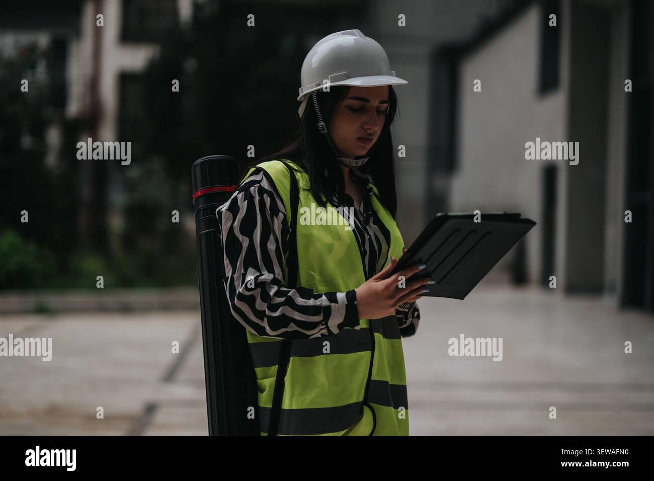 Female engineer on construction site wearing hard hat and high-visibility vest while using a tablet Stock Photo