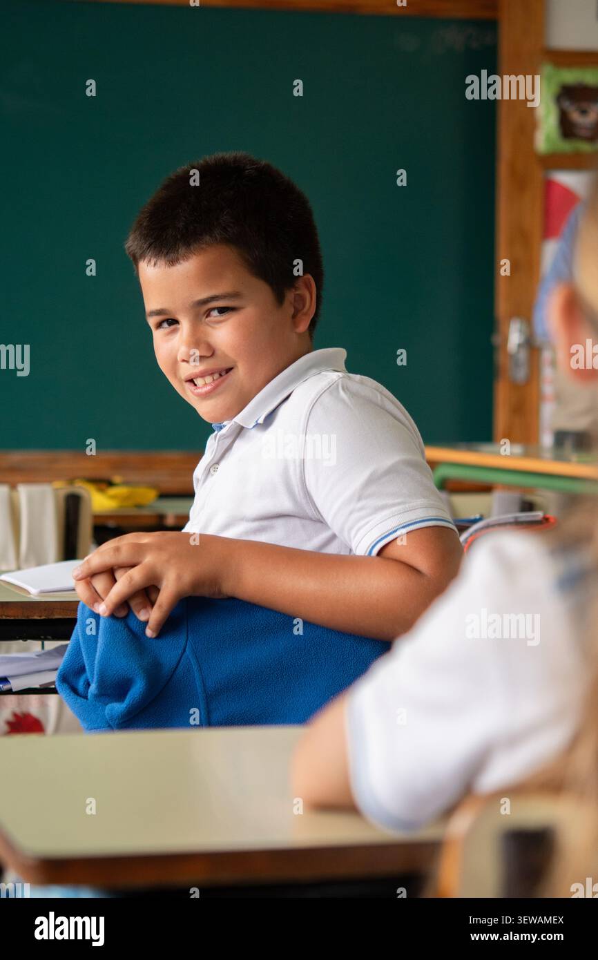 Elementary school boy smiling at classmate in classroom during lesson Stock Photo