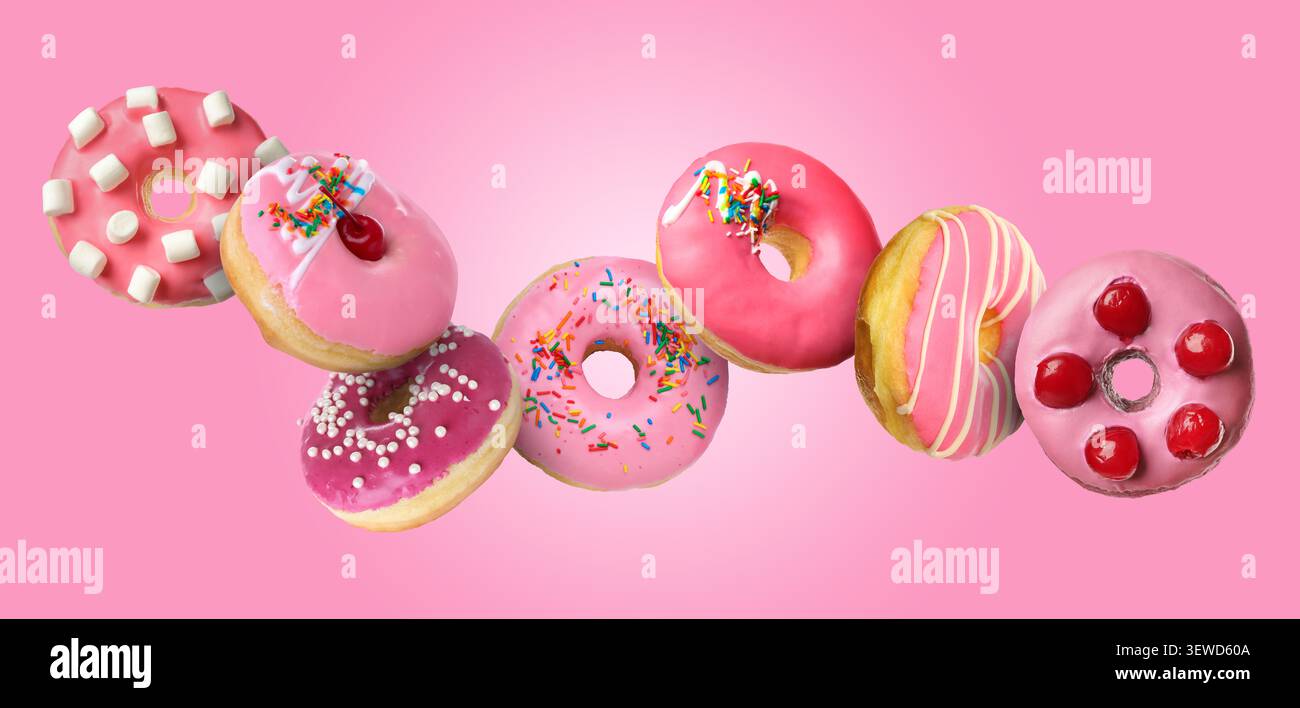 Sweet donuts covered with icing falling on pink background Stock Photo