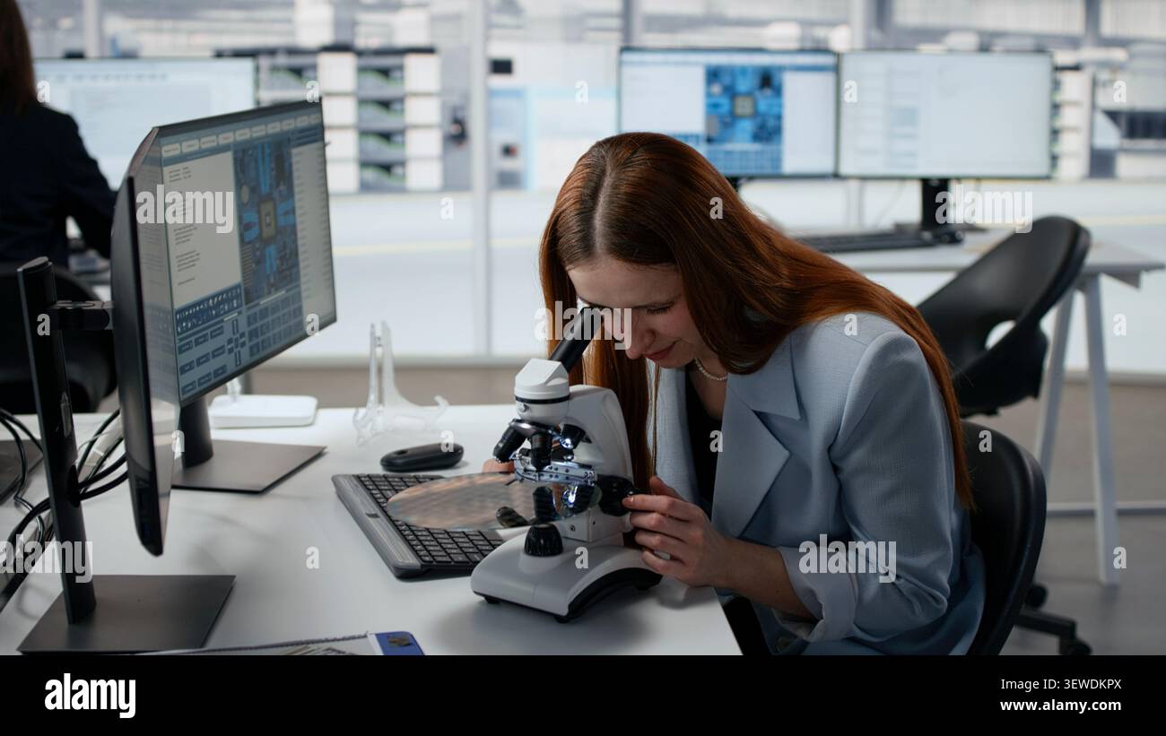 Woman using microscope in office, reviewing semiconductor substrate structures. Female materials scientists analyzing silicon wafer with optical device in industrial plant RD workspace, camera A Stock Photo