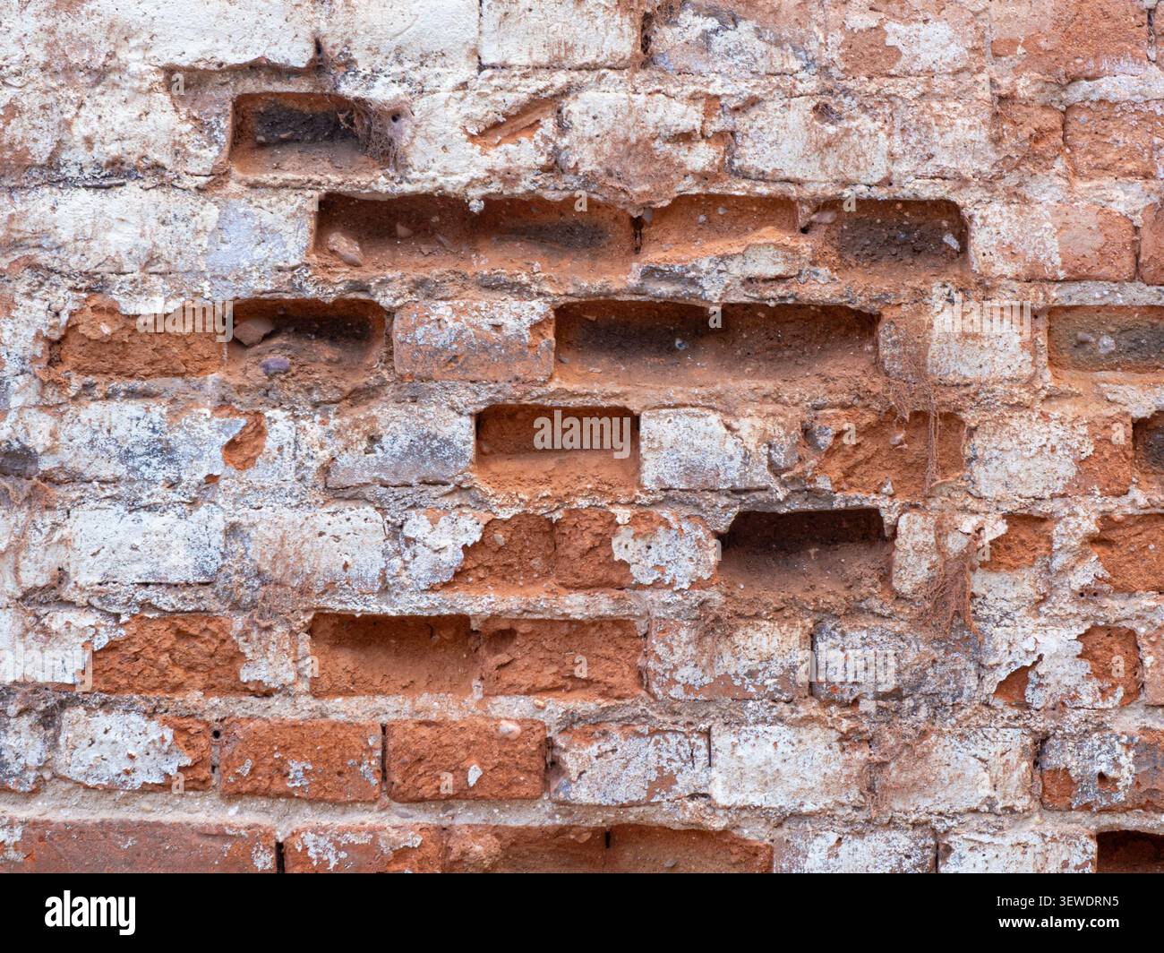 Old brick wall with peeling paint and missing bricks creating a weathered texture Stock Photo