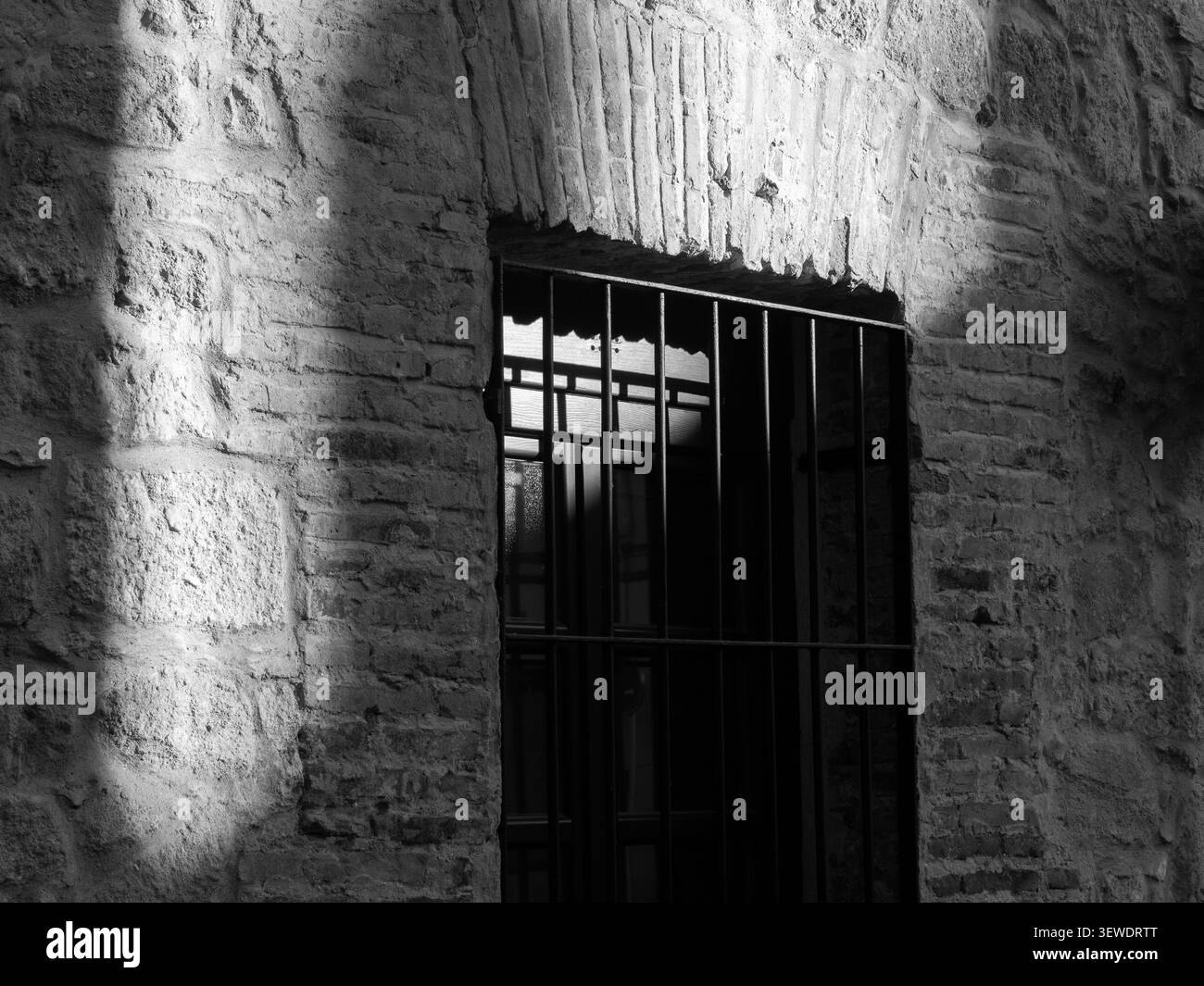 Stone wall framing a barred window, light and shadow creating contrast Stock Photo
