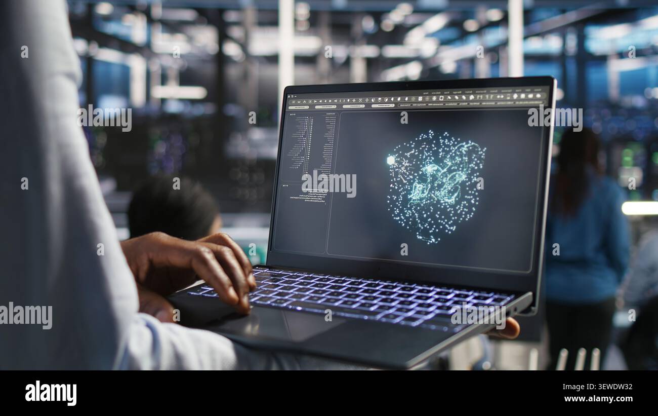 Data center technician monitors AI systems and machine learning workloads on a laptop inside a high-tech server facility. Stock Photo