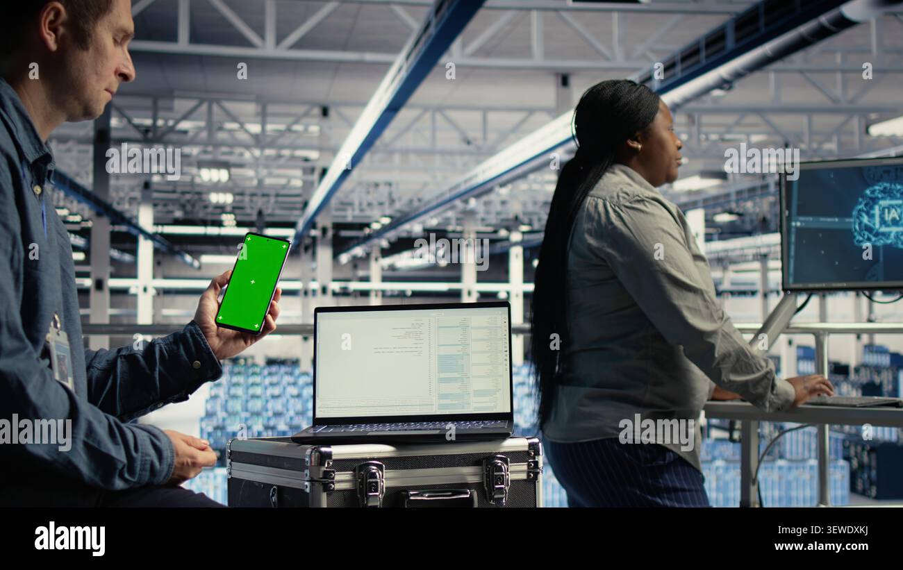 Software developer uses a green screen smartphone in a server room while waiting for code updates to finish. Stock Photo