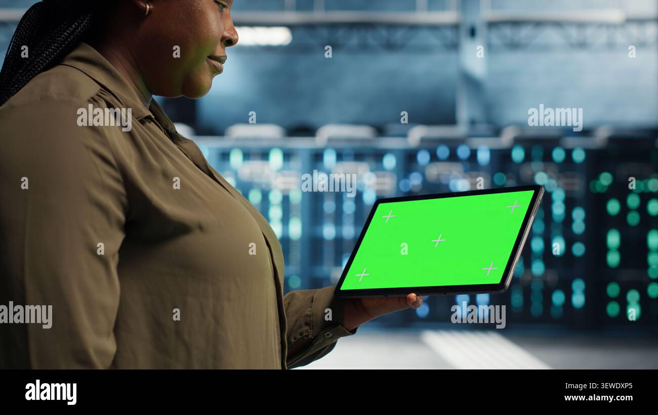 Software developer uses a green screen tablet in a server room for AI workflow and screen replacement. Stock Photo