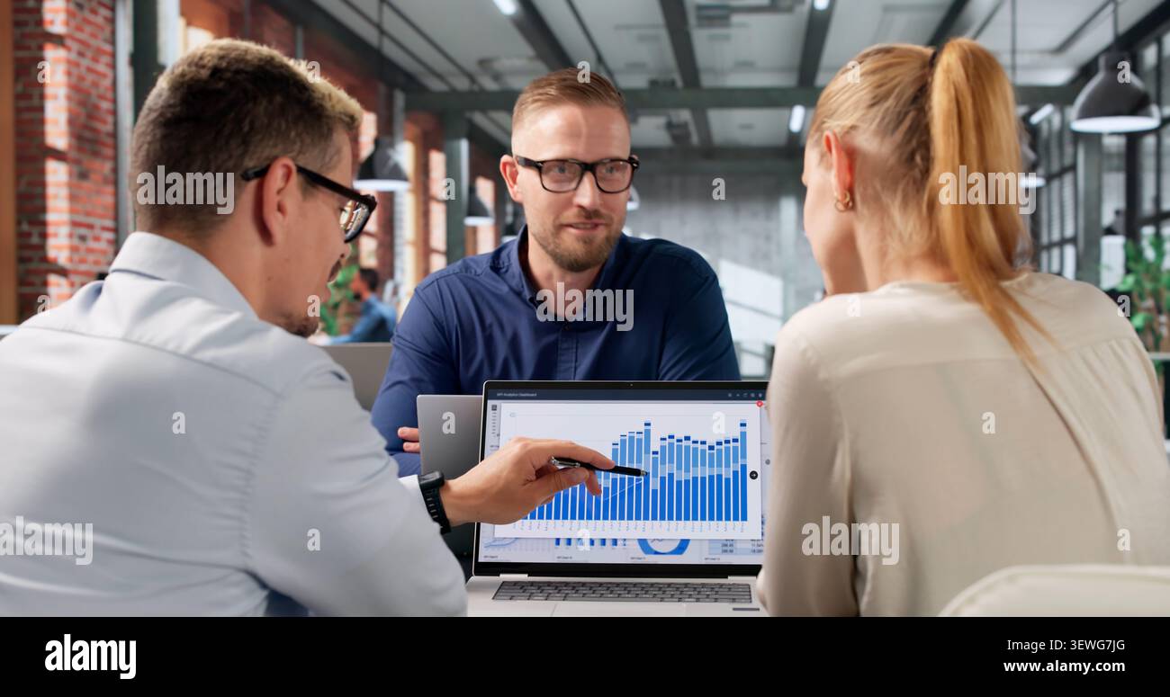 Two Financial Analysts Collaborate On KPI Dashboard Using Laptop Together. Stock Photo