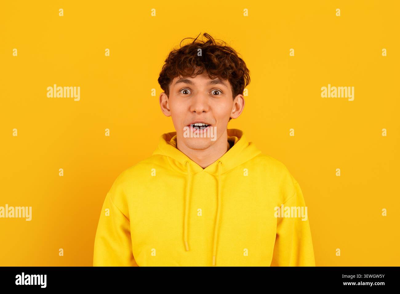 Surprised young man in yellow hoodie with wide eyes and open mouth Stock Photo