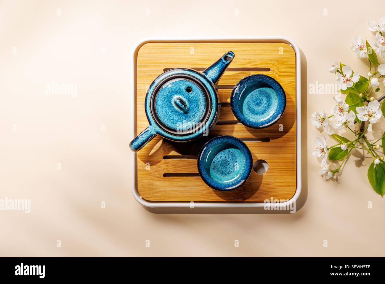 Blue ceramic teapot with blooming spring branch on wooden tray in minimal asian style composition Stock Photo