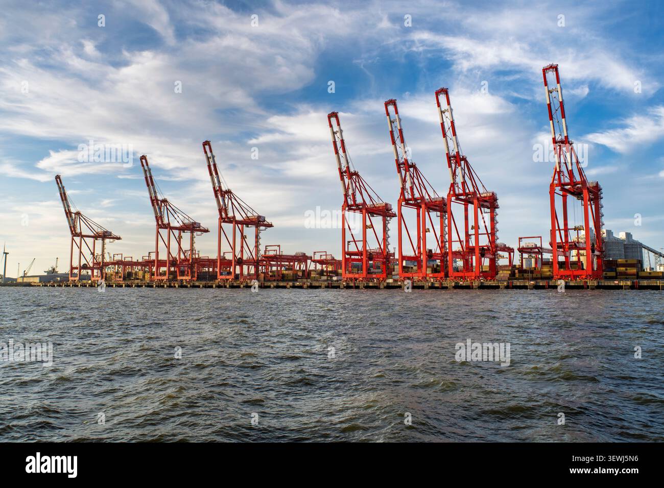 Tall red cranes line the edge of Seaforth docks, their arms stretched towards a blue sky. They are patiently awaiting the arrival of a ship to begin u Stock Photo