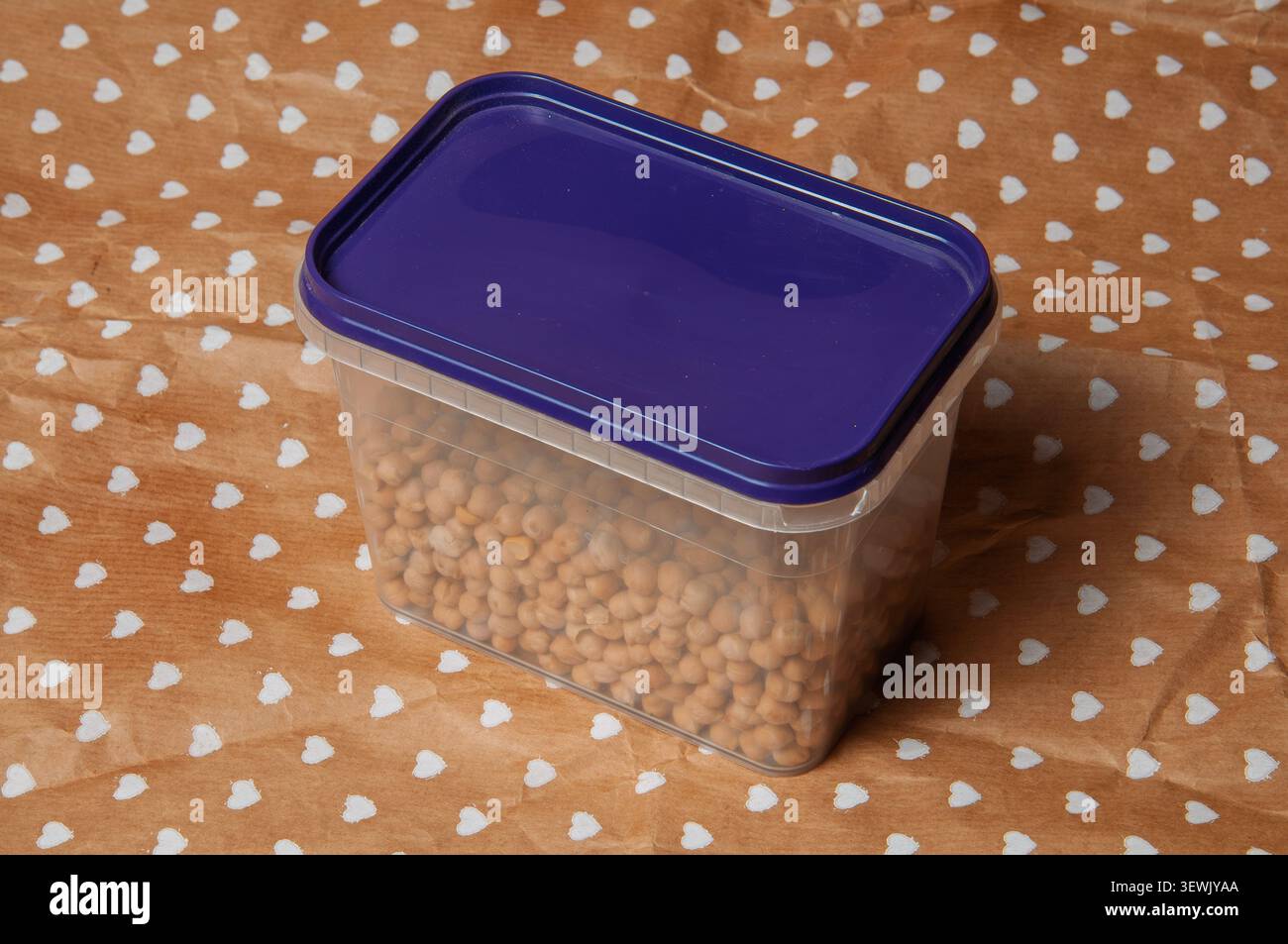 Clear plastic container filled with dried chickpeas on a brown paper with white hearts Stock Photo