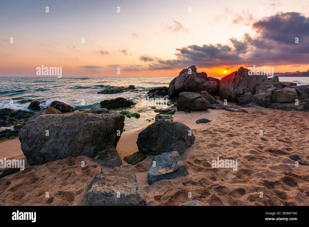 huge stones on a sandy beach at sunrise. wonderful summer vacation season at the black sea. calm waves washing the sand shore. nature background with Stock Photo