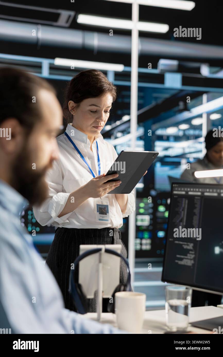 Data center engineer uses a digital tablet in a data center to manage AI virtualization and optimize server infrastructure. Stock Photo