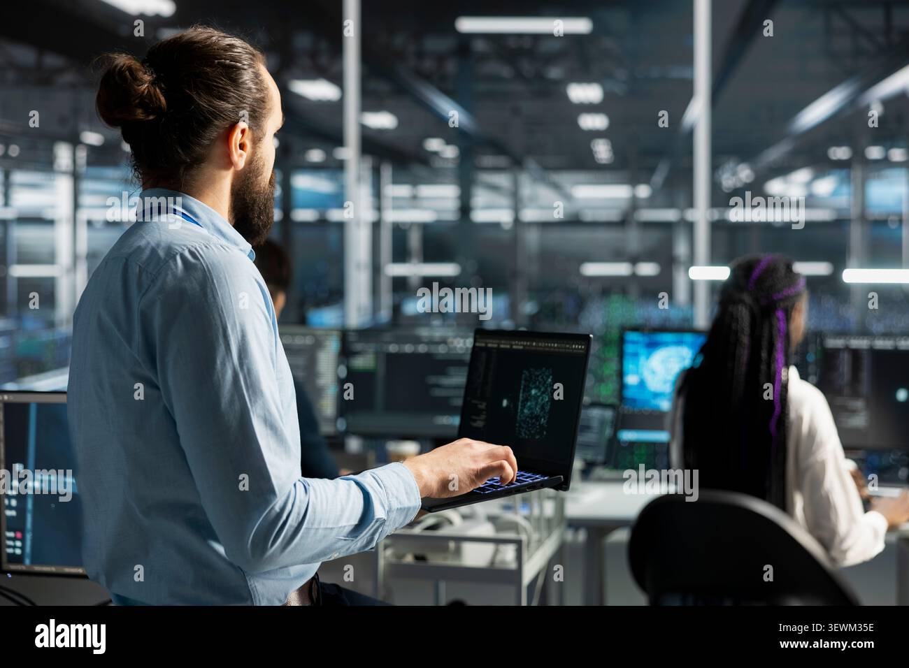 Data center engineer uses a laptop to manage AI training datasets and database workflows inside a server room. Stock Photo