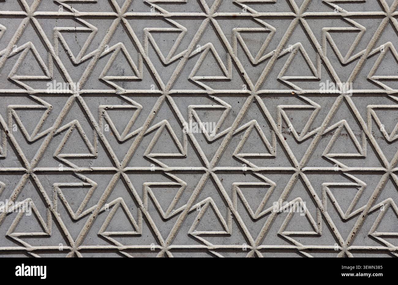 Geometric carved stone wall pattern featuring interconnected triangular and abstract interlocking shapes in grey concrete Stock Photo