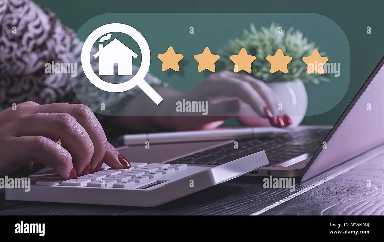 A businesswoman's hands are seen using a calculator and laptop, overlaid with a futuristic graphic of a house inside a magnifying glass next to a five Stock Photo