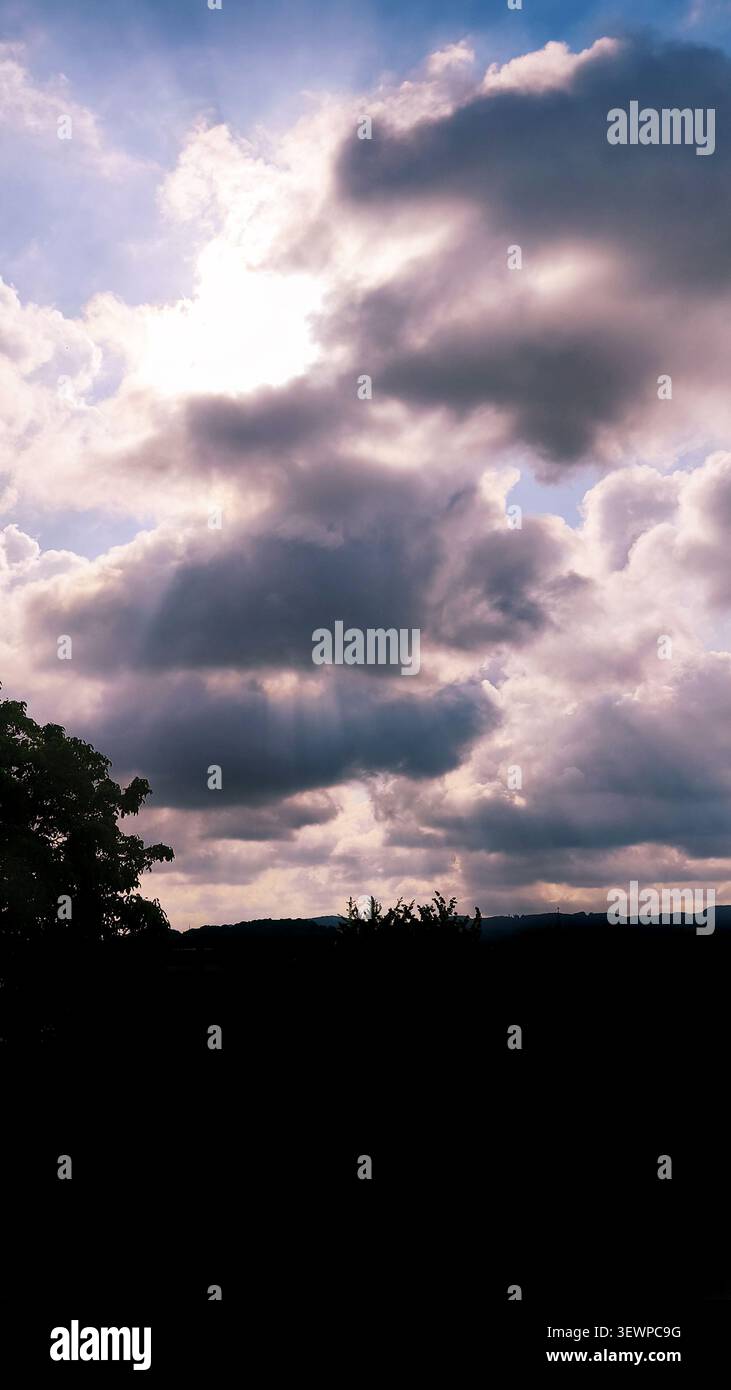 Sun rays breaking through dramatic storm clouds above a silhouetted landscape. Stock Photo